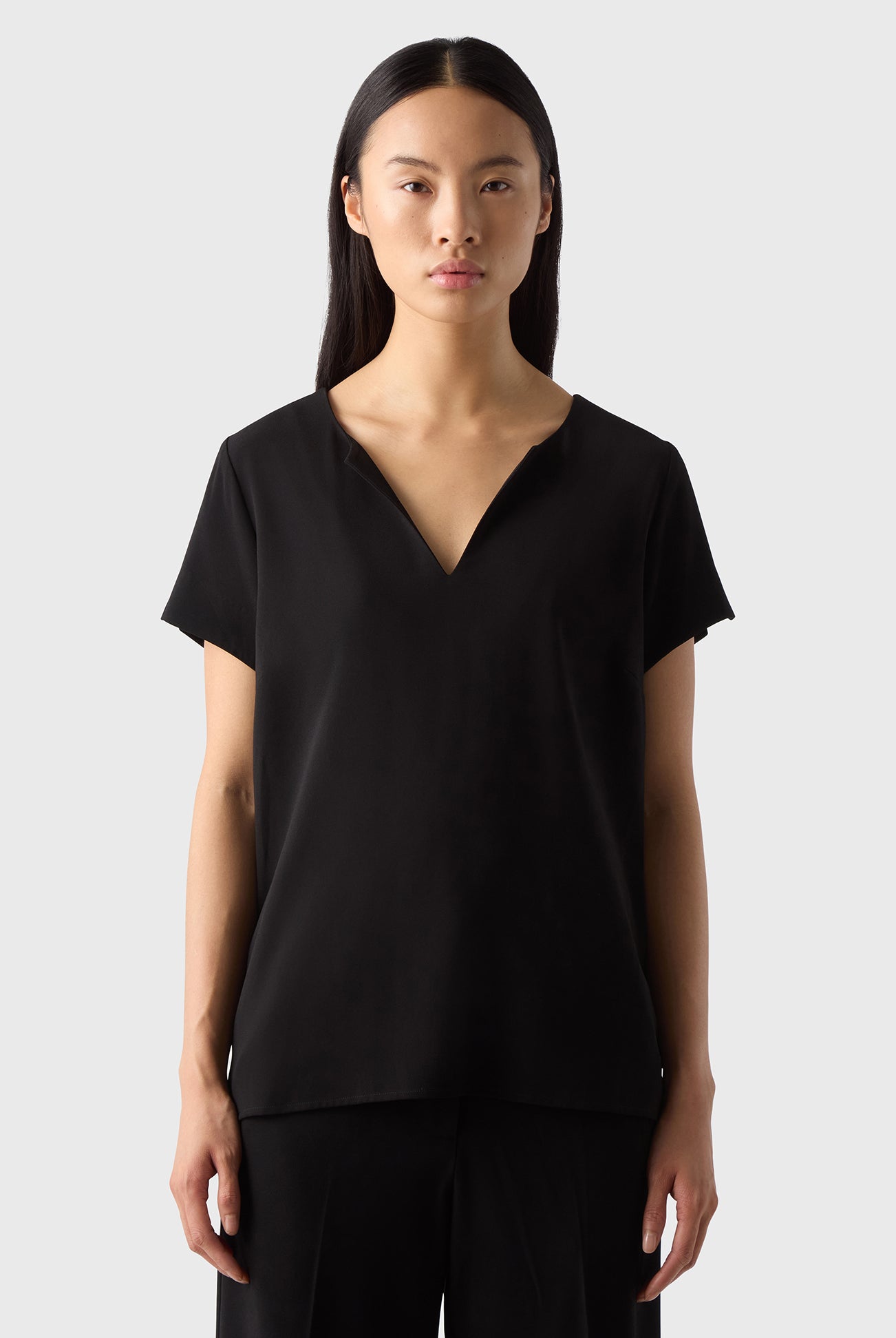 A woman wearing a black V-neck top with short sleeves, made of soft crèpe fabric, paired with black pants.